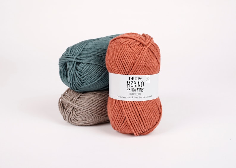 May include: Three balls of yarn in different colors: teal, brown, and orange. The orange ball has a label that reads "DROPS MERINO EXTRA FINE UNI COLOUR Superwash treated extra fine merino wool"