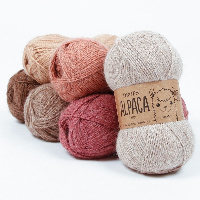 May include: A collection of six skeins of Drops Alpaca Mix yarn in various shades of brown, pink, and beige. The yarn is soft and fluffy, and the skeins are arranged in a pile. The label on the front skein reads "Drops Alpaca Mix - For all-time favorites!"