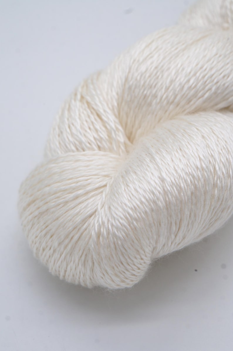 May include: A close-up of a skein of off-white yarn. The yarn is tightly wound, showing a textured surface. The fibers appear soft and have a slight sheen, suggesting a natural fiber like silk or linen. Ideal for knitting or crochet projects.