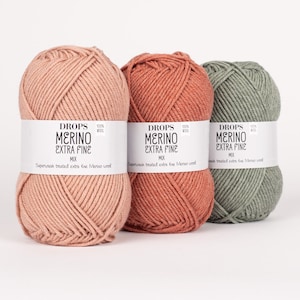 May include: Three skeins of Drops Merino Extra Fine yarn in the colors dusty rose, burnt orange, and sage green. The yarn is 100% wool and is superwash treated.