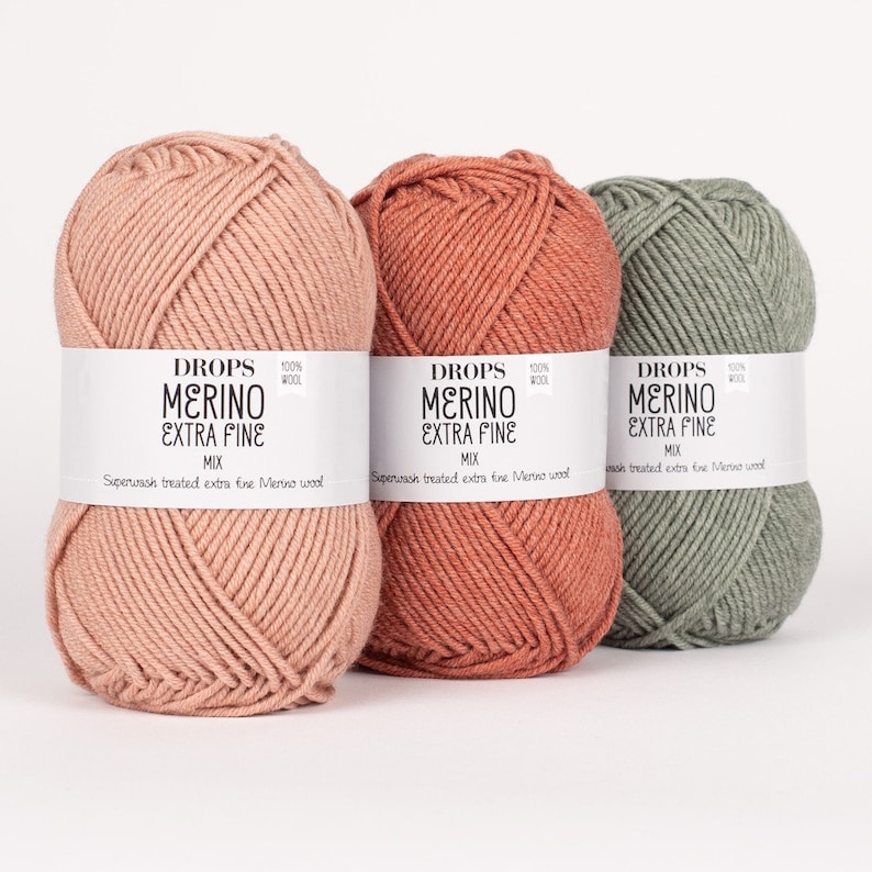 May include: Three skeins of Drops Merino Extra Fine yarn in the colors dusty rose, burnt orange, and sage green. The yarn is 100% wool and is superwash treated.