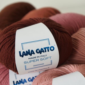 Puede incluir: Primer plano de una madeja de lana marr&oacute;n con una etiqueta blanca que dice "Lana Gatto Made in Italy Super Soft www.lanagatto.it".