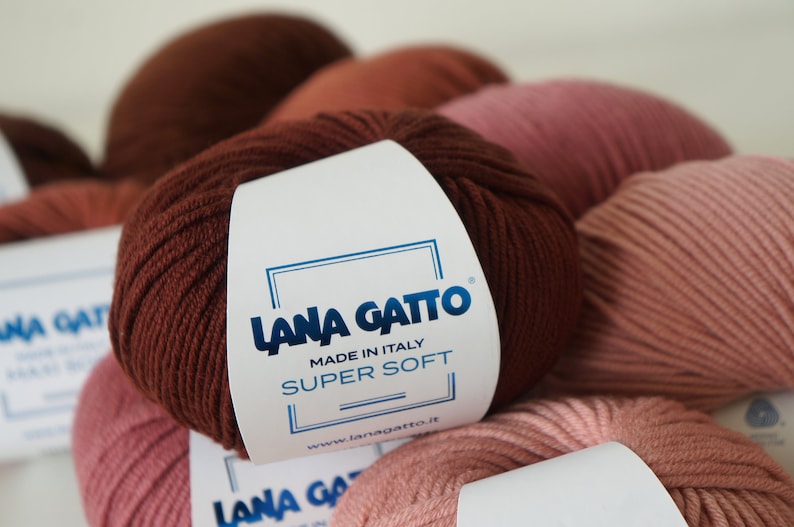 Puede incluir: Primer plano de una madeja de lana marr&oacute;n con una etiqueta blanca que dice "Lana Gatto Made in Italy Super Soft www.lanagatto.it".