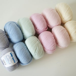 Puede incluir: Diez ovillos de lana en varios colores pastel, incluyendo azul claro, verde p&aacute;lido, rosa y crema. La lana est&aacute; etiquetada como "Lana Gatto Super Soft".
