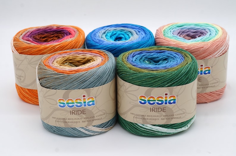 Puede incluir: Cinco ovillos de hilo Sesia Iride en diferentes combinaciones de colores. El hilo es 100% algod&oacute;n org&aacute;nico y est&aacute; disponible en una variedad de colores. El hilo est&aacute; empaquetado en un tubo de cart&oacute;n con una etiqueta que dice "Sesia Iride" y "100% cotone biologico - organic cotton - coton biologique - bio baumwolle".