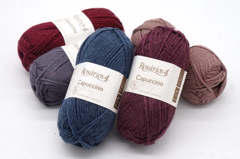 May include: Six balls of yarn in various colours, including burgundy, grey, blue, and brown. Each ball has a label that reads "Ros&aacute;rios 4 Cappuccino" and "Exclusively Collection".