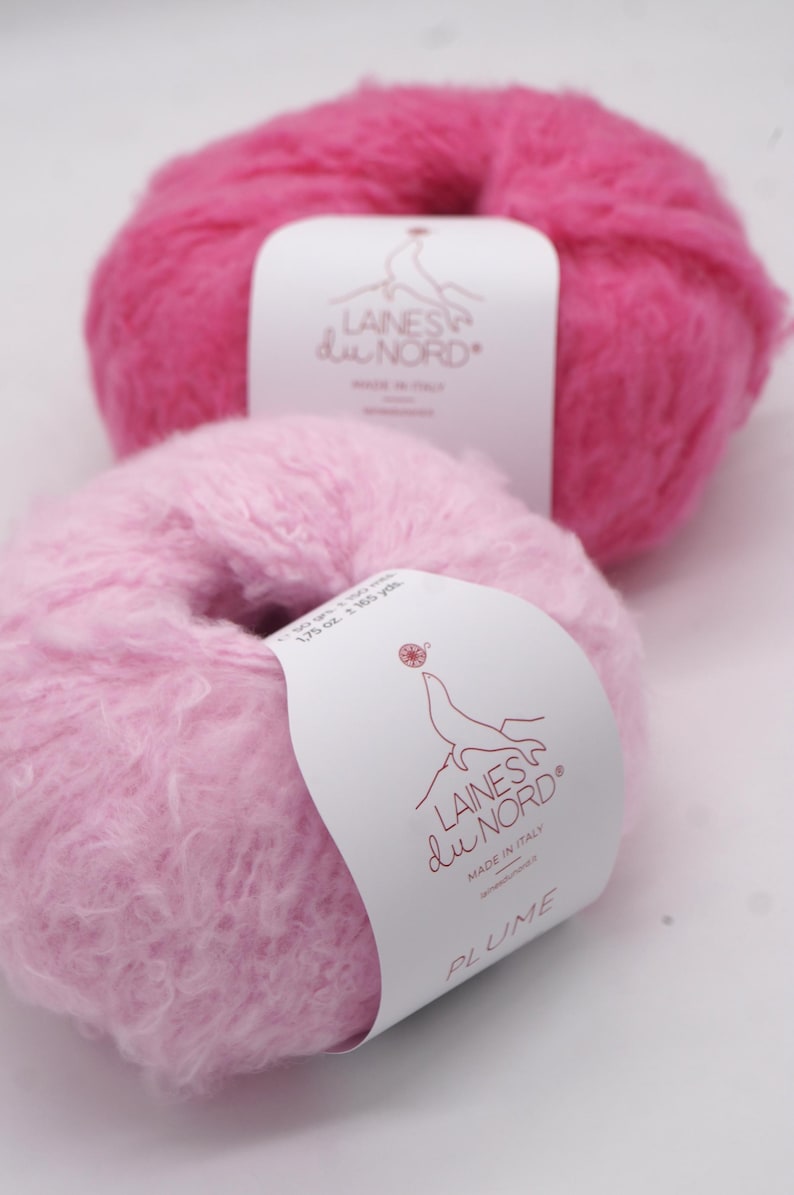 Pu&ograve; includere: Due gomitoli di lana rosa soffice. Il gomitolo superiore &egrave; fucsia vibrante, mentre quello inferiore &egrave; rosa pastello pi&ugrave; chiaro. Ogni gomitolo ha un'etichetta con il testo "LAINES du NORD" e "MADE IN ITALY". Il gomitolo inferiore &egrave; etichettato "PLUME".