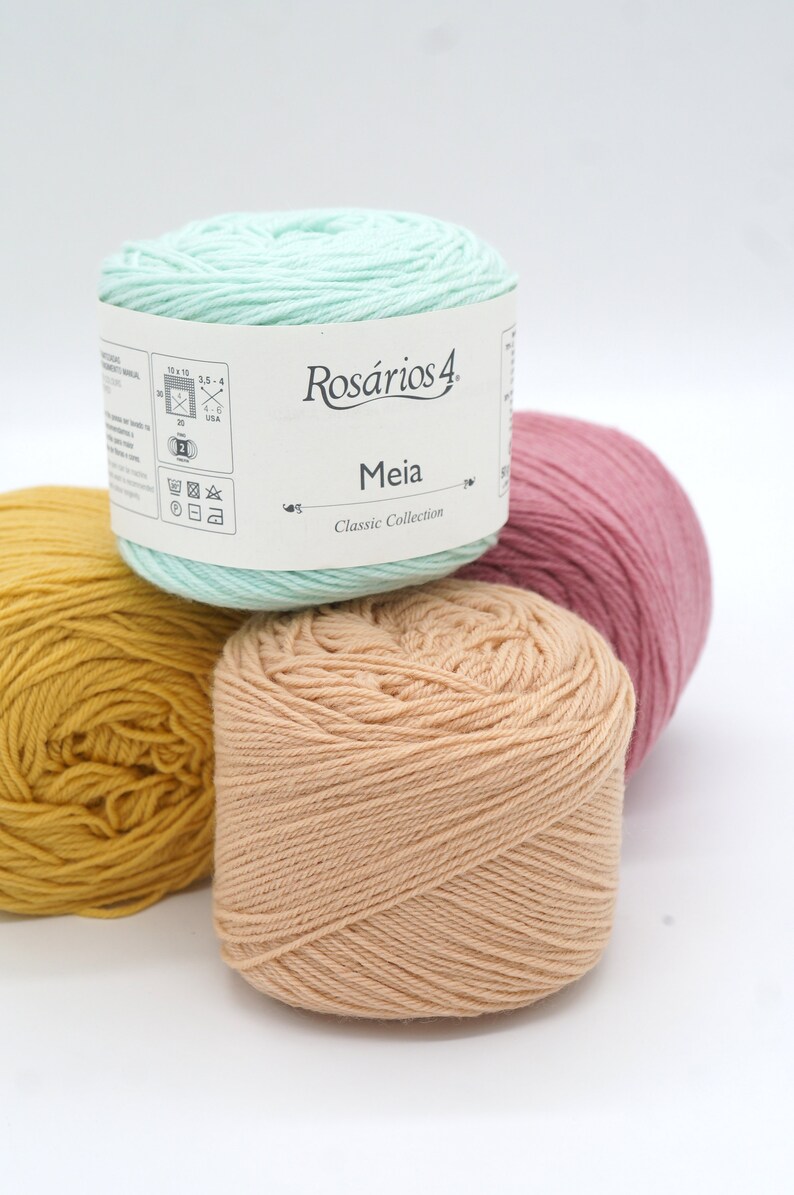 May include: Four balls of yarn in different colors: yellow, peach, light green, and pink. The light green ball has a label that says "Ros&aacute;rios 4 Meia Classic Collection".