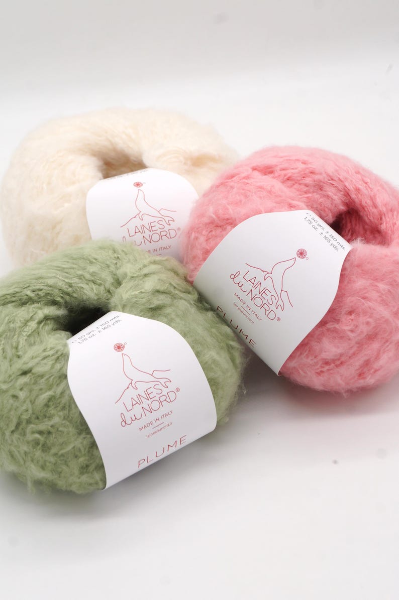 Pu&ograve; includere: Tre gomitoli di filato soffice in crema, rosa e verde. Ogni gomitolo ha un'etichetta con la scritta "LAINES du NORD" e "PLUME". Il filato &egrave; morbido e sembra essere un misto mohair, perfetto per progetti di maglia o uncinetto.