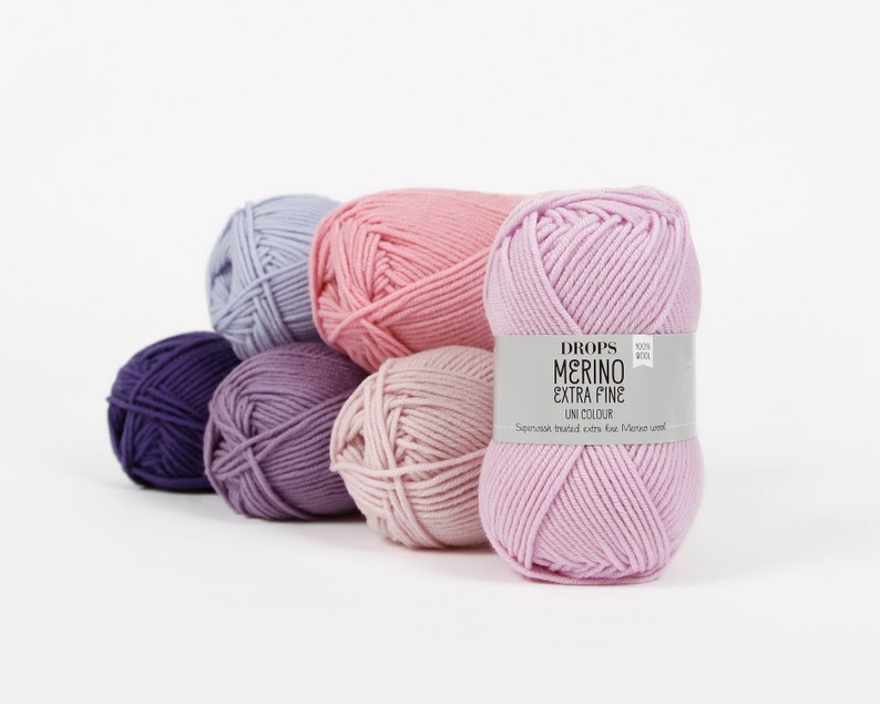 May include: Six balls of yarn in various shades of pink and purple. The yarn is labeled "DROPS MERINO EXTRA FINE UNI COLOUR 100% WOOL" and "Superwash treated extra fine Merino wool."
