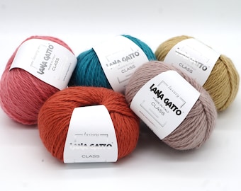Può includere: Cinque gomitoli di lana in diversi colori: rosa, arancio, turchese, beige e rosa chiaro. Ogni gomitolo ha un'etichetta bianca con il testo "luxury LANA GATTO MADE IN ITALY CLASS" stampato su di essa.