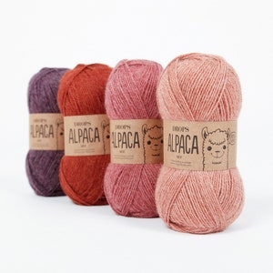 May include: Four skeins of yarn in different shades of pink, red, and purple. Each skein has a label that reads "DROPS ALPACA MIX" with a cartoon alpaca on it.