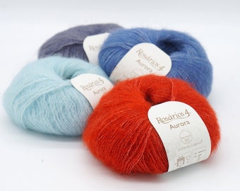 Puede incluir: Cuatro ovillos de hilo en diferentes colores: azul claro, rojo, azul y gris. Cada ovillo tiene una etiqueta que dice "Rosarios 4 Aurora" y "Botanically Collection".