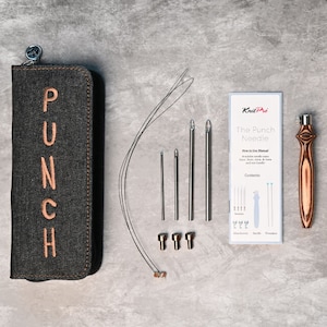 May include: A denim-style case with the word "PUNCH" embroidered in tan, a set of silver punch needles, and a wooden punch needle tool. The set includes a "KnitPro" instruction manual and various attachments. The tools are arranged on a grey surface.