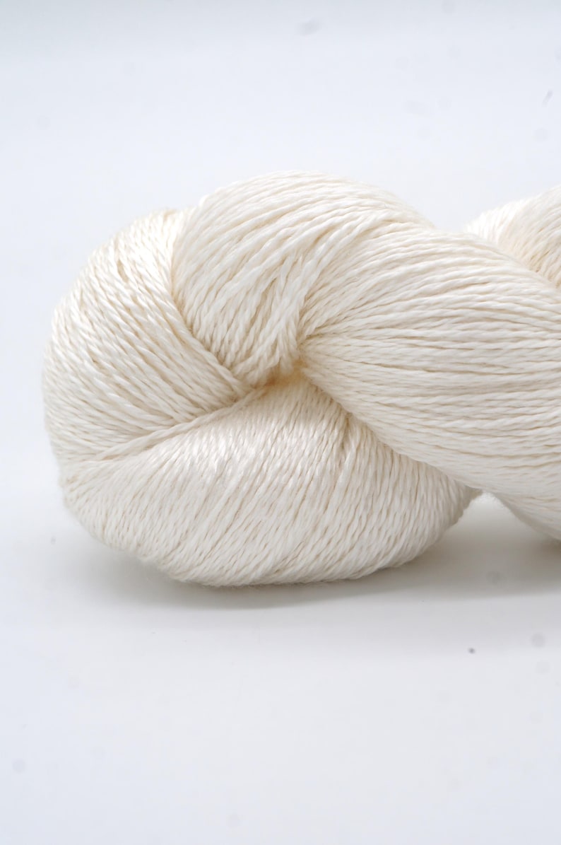 May include: A close-up of a skein of off-white yarn. The yarn is tightly wound, with visible strands and a soft, textured appearance. The yarn is likely used for knitting or crocheting projects.