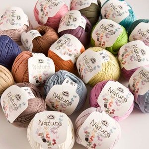 May include: A collection of 18 balls of yarn in various colors, including pink, green, blue, orange, and beige. Each ball has a label that reads "Natura Just Cotton".