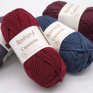 May include: Four skeins of yarn in different colours: dark purple, dark blue, red, and grey. Each skein has a label that reads "Ros&aacute;rios 4 Cappuccino" and "Eco-friendly Collection".