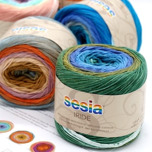 Puede incluir: Primer plano de un ovillo de hilo verde, azul y beige con el nombre de la marca "sesia iride" y el texto "100% cotone biologico - organic cotton - coton biologique - bio baumwolle" en la etiqueta.