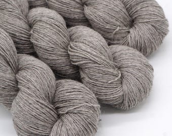 May include: Close-up of several skeins of gray yarn. The yarn is tightly wound, showing the texture of the fibers. The color is a neutral gray, suitable for various knitting or crochet projects.