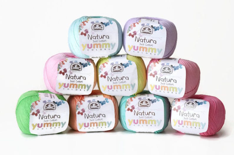 K&ouml;nnte beinhalten: Neun Kn&auml;uel DMC Natura Just Cotton Yummy Colors Garn in verschiedenen Pastellfarben, darunter Rosa, Gr&uuml;n, Blau und Gelb.