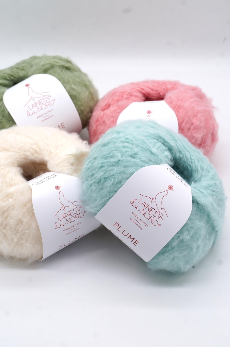 Pu&ograve; includere: Una collezione di gomitoli di lana colorati nei toni del verde, rosa, crema e blu. Ogni gomitolo ha un'etichetta con il testo "LAINES du NORD" e "PLUME". La lana &egrave; soffice e sembra morbida.