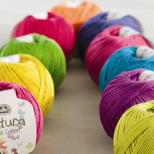 May include: A row of colorful yarn balls in shades of pink, yellow, green, blue, and purple. The yarn is labeled "Natura Just Cotton" and is made by DMC.
