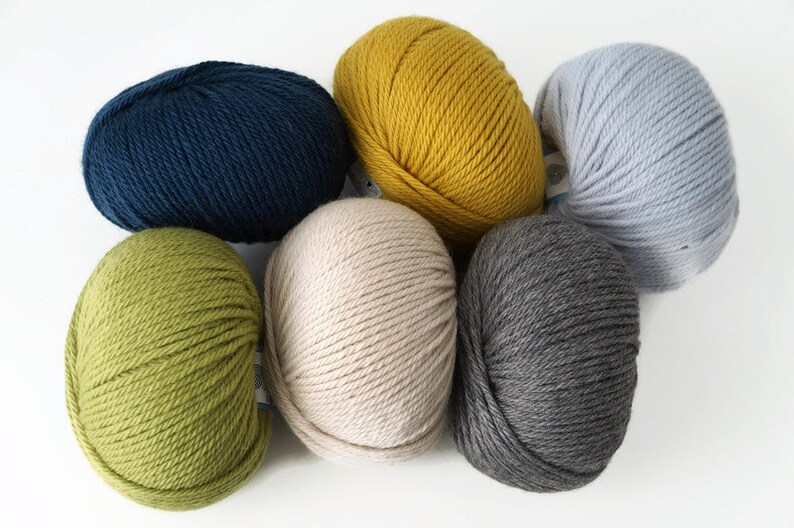 May include: Six balls of yarn in different colors: green, yellow, blue, gray, beige, and light blue. The yarn is arranged in a circle.