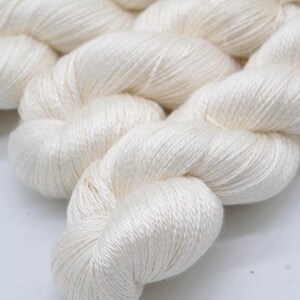 May include: Close-up of a skein of off-white yarn. The yarn is tightly twisted, with a soft, slightly shiny texture. The yarn is likely made of natural fibers, such as silk or cotton, and is suitable for knitting or crocheting projects.