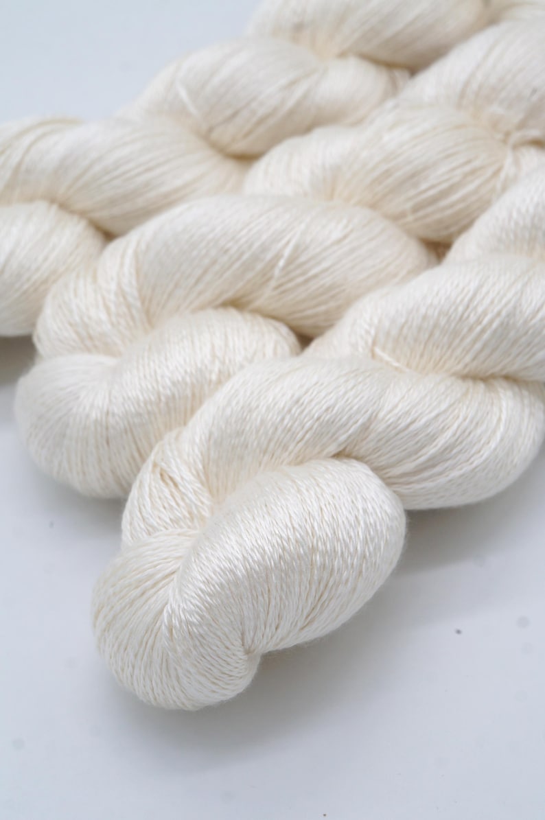 May include: Close-up of a skein of off-white yarn. The yarn is tightly twisted, with a soft, slightly shiny texture. The yarn is likely made of natural fibers, such as silk or cotton, and is suitable for knitting or crocheting projects.