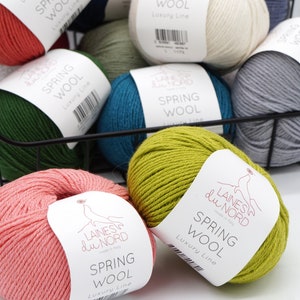 May include: A basket filled with balls of yarn in various colors, including green, blue, pink, white, and yellow. Each ball has a label that reads "Laines du Nord" and "Spring Wool Luxury Line".