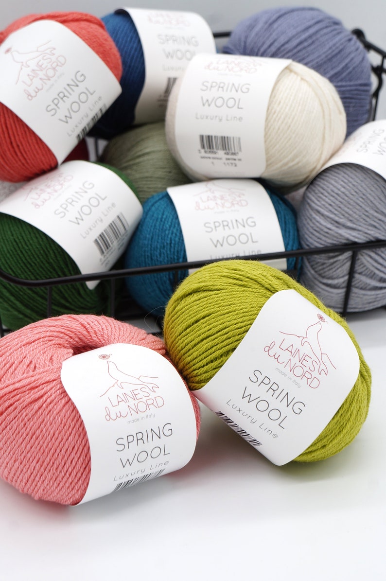 May include: A basket filled with balls of yarn in various colors, including green, blue, pink, white, and yellow. Each ball has a label that reads "Laines du Nord" and "Spring Wool Luxury Line".