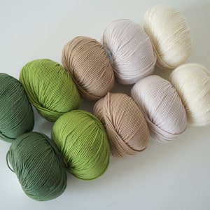 Puede incluir: Ocho ovillos de lana en varios tonos de verde, beige y blanco. La lana est&aacute; dispuesta en un degradado de verde oscuro a blanco.