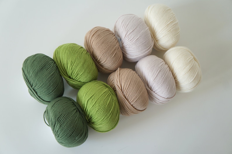 Puede incluir: Ocho ovillos de lana en varios tonos de verde, beige y blanco. La lana est&aacute; dispuesta en un degradado de verde oscuro a blanco.
