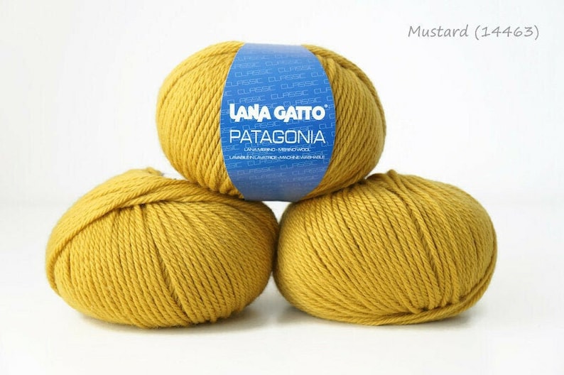 May include: Three balls of mustard yellow yarn, labeled "Lana Gatto Patagonia" on the blue label of the top ball.