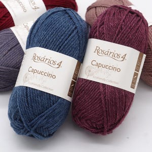 May include: Four balls of yarn in different colours: red, pink, blue, and burgundy. Each ball has a label that says "Ros&aacute;rios 4. Capuccino Ecofriendly Collection".