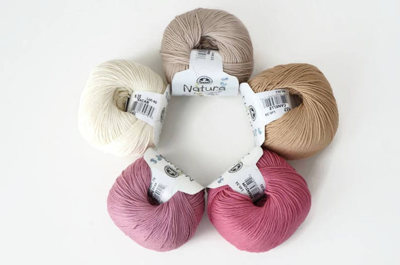 May include: Five balls of yarn in different colors: beige, white, light brown, pink, and a darker shade of pink. Each ball has a label with the word "Natura" printed on it.