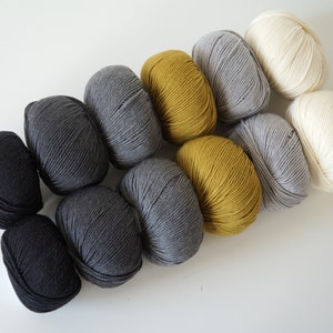 Puede incluir: Una colecci&oacute;n de ovillos de lana en negro, gris, amarillo y blanco. La lana est&aacute; dispuesta en un degradado de oscuro a claro.