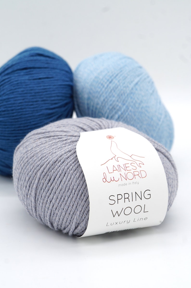 May include: Three skeins of yarn, one gray, one light blue, and one dark blue. The gray skein has a white label that reads "Laines du Nord made in Italy Spring Wool Luxury Line".