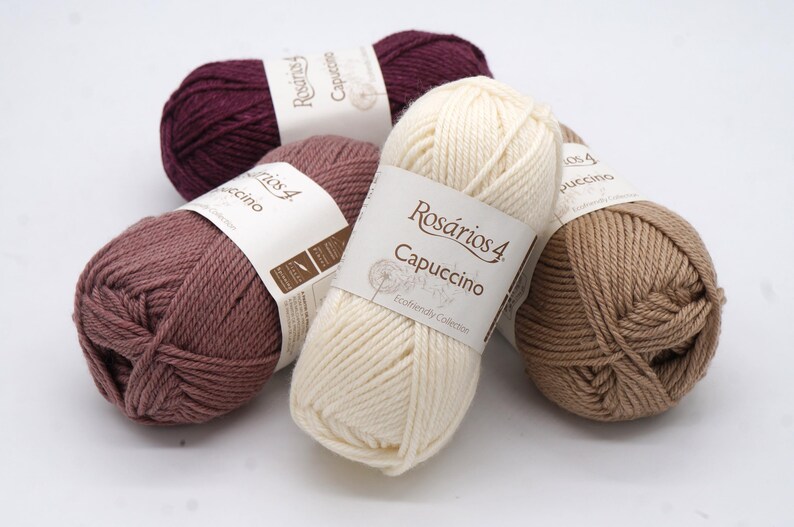 May include: Four balls of yarn in different colours: burgundy, light brown, beige, and a light pink. The yarn is labelled "Rosarios 4 Cappuccino" and "Eco-friendly Collection".