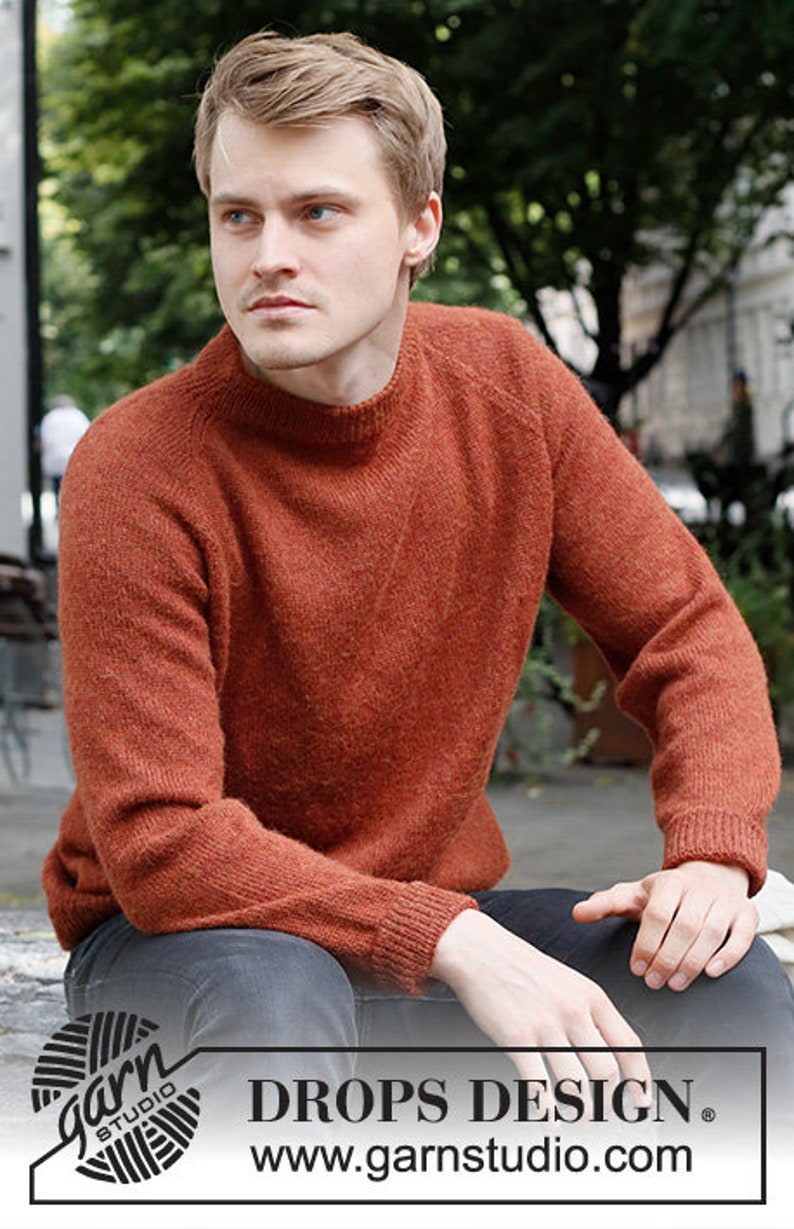 May include: A rust-colored sweater with a round neckline and long sleeves. The sweater is made of a soft, fuzzy material. The text "DROPS DESIGN" and "www.garnstudio.com" is visible at the bottom of the image.