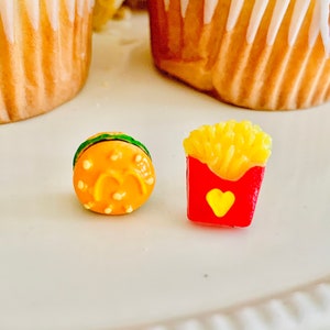 May include: Miniature burger and fries set. The burger is orange with a green top and the letter "M" on it. The fries are yellow and in a red container with a yellow heart.