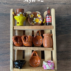 May include: A miniature wooden shelf displays various handcrafted ceramic items. The shelf holds a yellow and brown teapot, a brown plate with yellow floral designs, and a small bottle. Other items include small mugs, a handled pot, and a black speckled bowl. The text "Style #2" is visible.