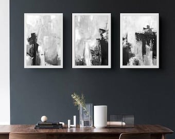 May include: Three framed abstract art pieces in black, white, and gray hang above a wooden dining table. The table is surrounded by wooden chairs with black metal legs. Decorative items, including a vase and candles, are on the table.