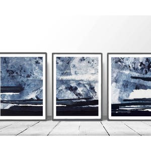 Pu&ograve; includere: Tre dipinti astratti incorniciati in tonalit&agrave; di blu e bianco. I dipinti sono in cornici nere e sono appesi a una parete bianca.