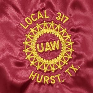 May include: A red fabric patch with gold embroidery. The embroidery reads "LOCAL 317 UAW HURST, TX."
