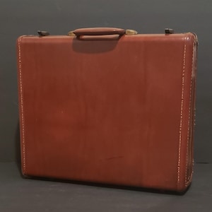 May include: A brown leather briefcase with a brass handle and metal clasps.