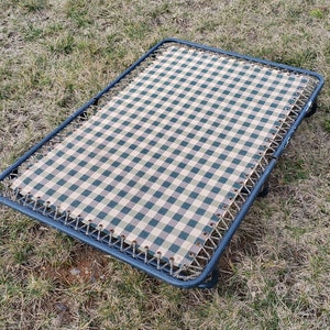 May include: A black metal cot with a checkered green and beige fabric stretched across the frame.