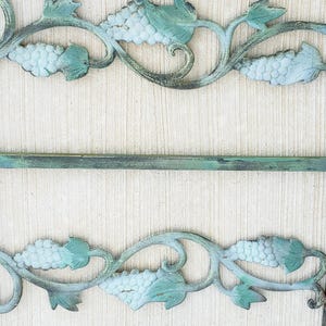 May include: A decorative metal grapevine design with a distressed green finish. The design features a repeating pattern of grapes and leaves.