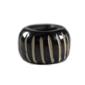 May include: A dark brown, cylindrical bead with vertical, cream-colored stripes. The bead has a rounded shape and a central hole, likely for stringing. The design is simple and elegant, suitable for jewelry making or crafts.