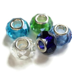 May include: Five faceted glass beads in shades of blue, green, and clear. Each bead has a silver-colored metal core. The beads are arranged on a white background, showcasing their jewel-like appearance.